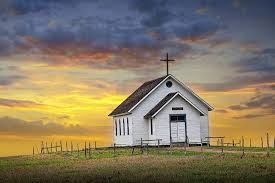 A picturesque white church with a cross at sunset, surrounded by grassy fields.